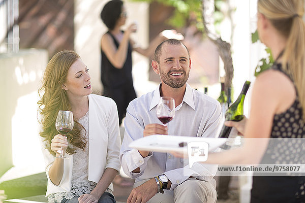 Waitress with tray and couple sitting outdoors tasting red wine