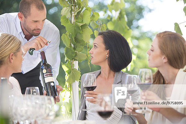 Kellnerin präsentiert den Frauen eine Flasche Rotwein bei einer Weinverkostung.