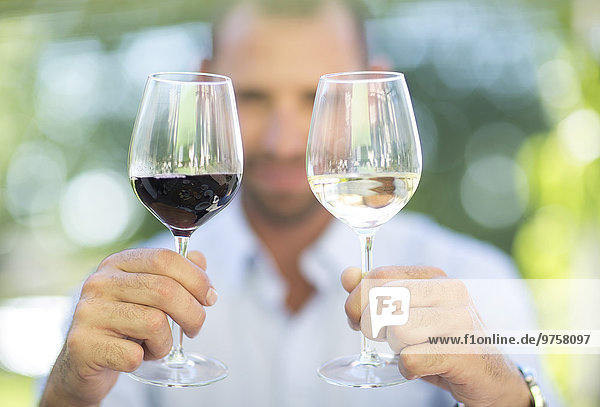 Mann vergleicht Weißwein und Rotwein bei einer Weinprobe