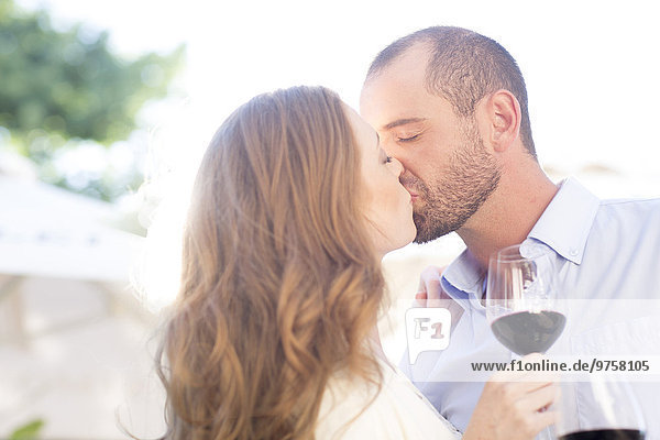 Couple holding wine glasses and kissing outdoors