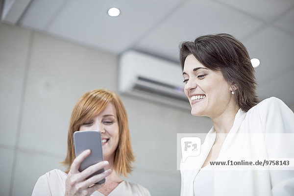 Zwei lächelnde Geschäftsfrauen beim Blick aufs Handy