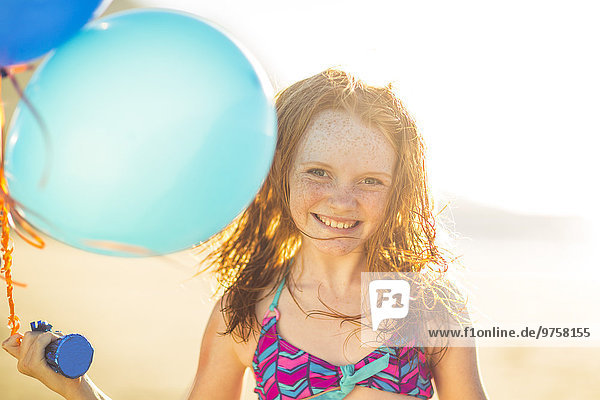 Mädchen am Strand lächelt und hält Luftballons