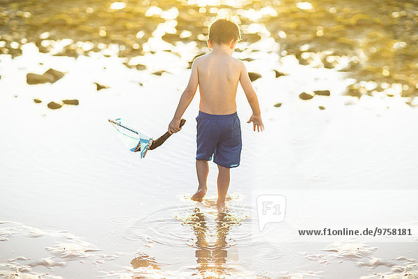 Boy wading with a toy wooden boat in the water