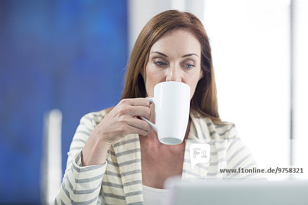 Geschäftsfrau im Büro beim Kaffeetrinken und Arbeiten am Laptop