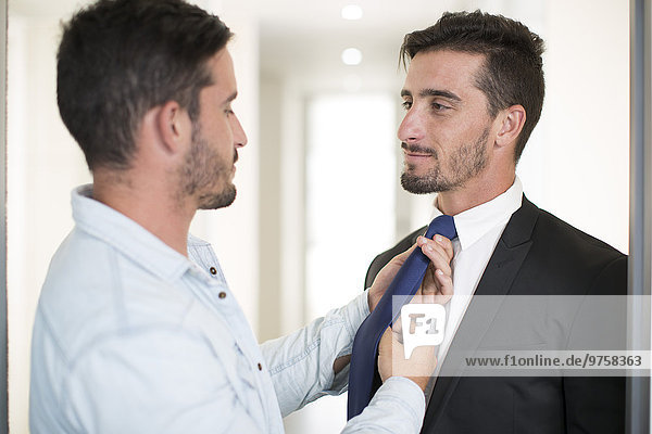 Casually dressed man adjusting tie of twin brother in office