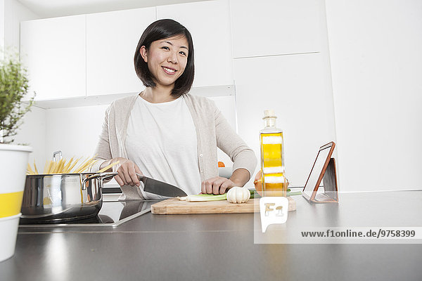 Porträt einer lächelnden jungen Frau beim Schneiden von Frühlingszwiebeln in der Küche