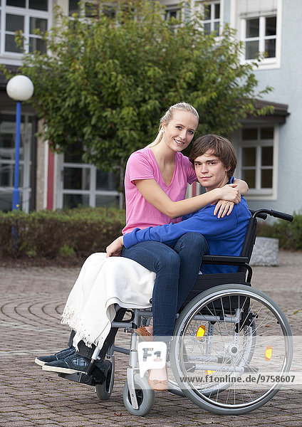 Junge Frau  die ihren Freund im Rollstuhl umarmt