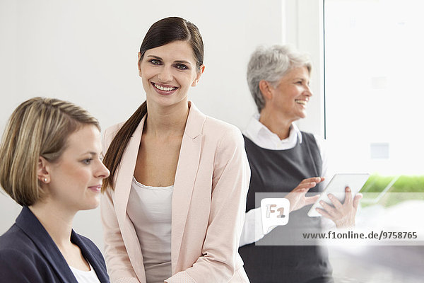 Three smiling businesswomen with digital tablet in office