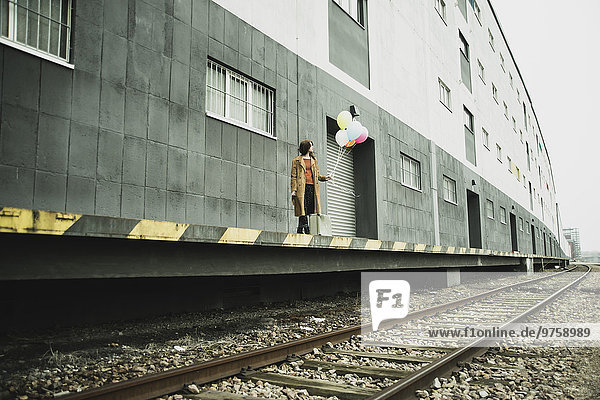 Junge Frau mit Koffer mit Ballonbund auf Plattform
