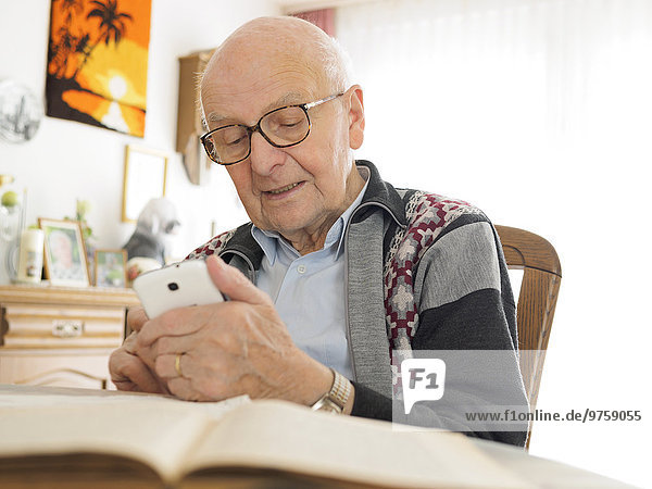 Old man sitting at table using cell phone