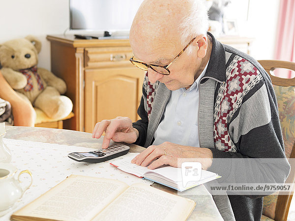 Old man sitting at table looking for telephone number in notebook