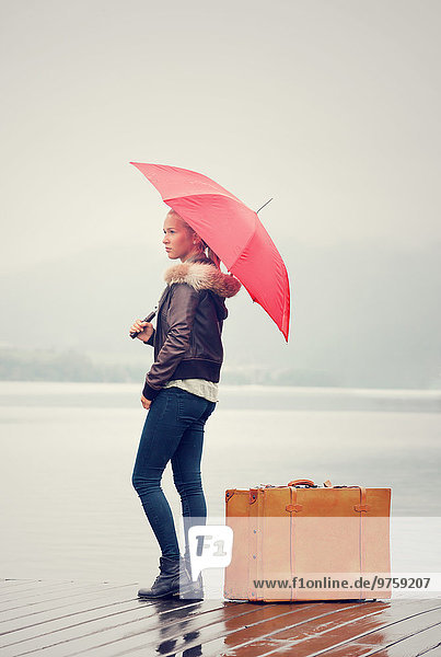 Österreich  Mondsee  Teenagermädchen mit rotem Regenschirm im Regen stehend mit Koffer