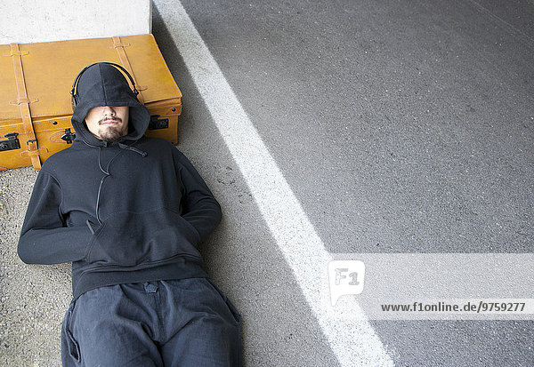 Mann mit Kapuzenjacke schläft neben der Bahn
