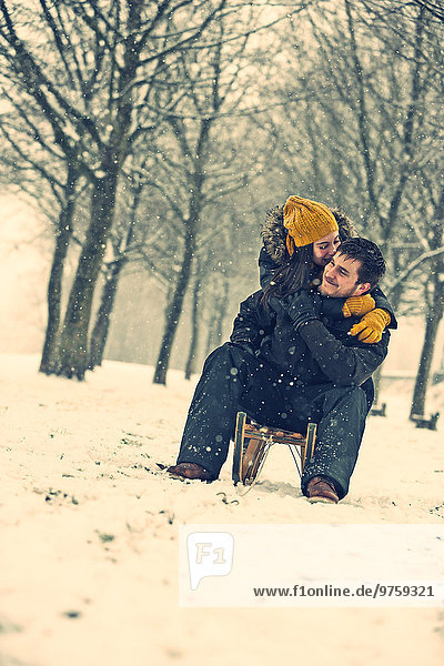 Verliebtes junges Paar auf einem Schlitten im Winter