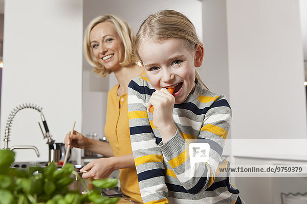 Mother with daughter eating carrot in kitchen
