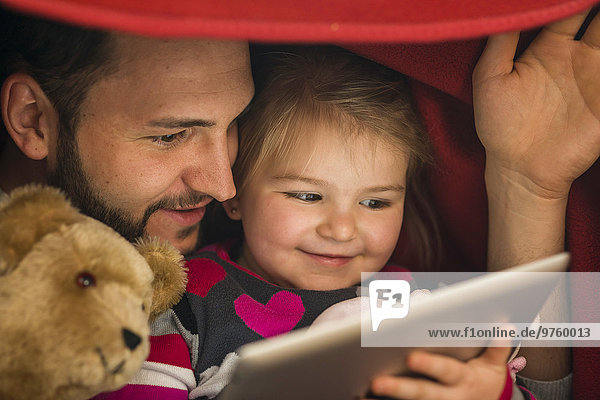 Vater und Tochter mit digitalem Tablett unter der Decke