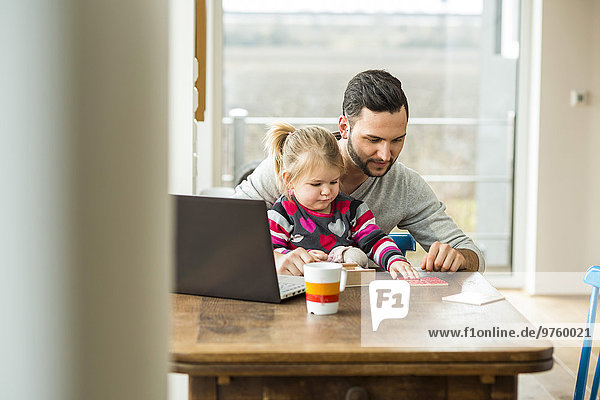 Vater und Tochter mit Laptop und Spiel am Holztisch