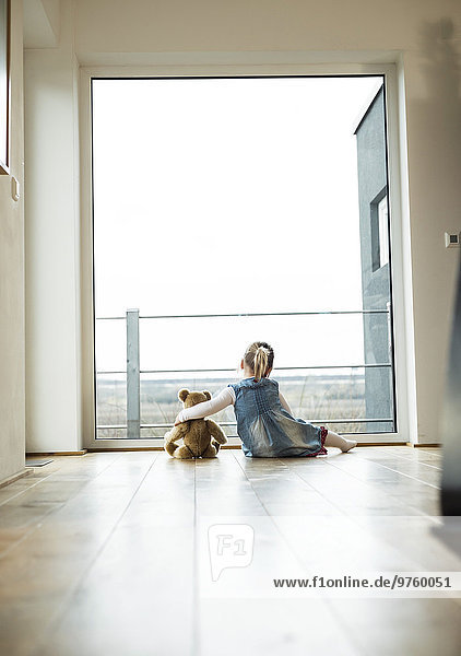 Girl sitting next to teddy looking out of window