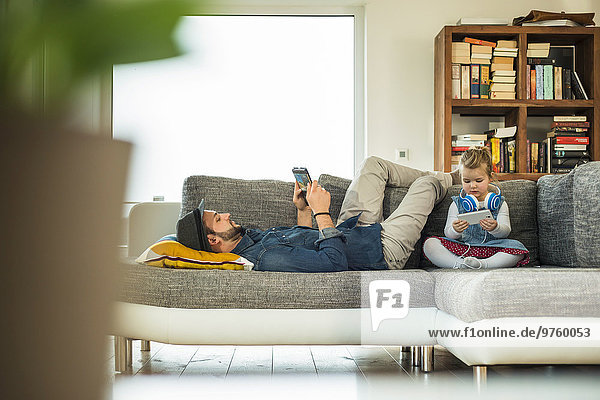 Vater und Tochter mit digitalem Tablett und Smartphone auf Sofa