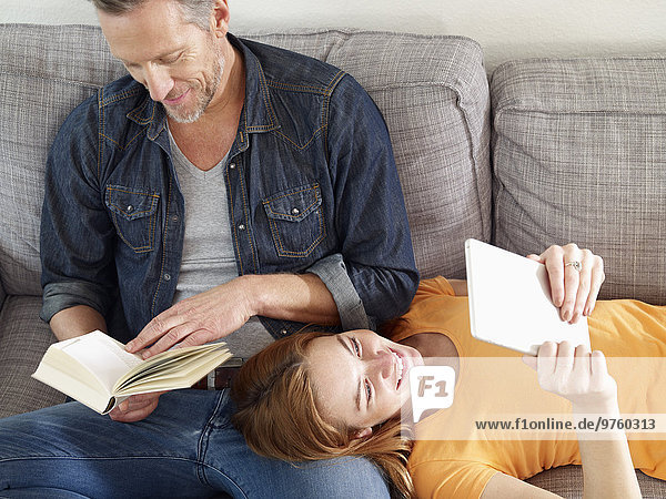 Mature man with adult daughter reading on sofa