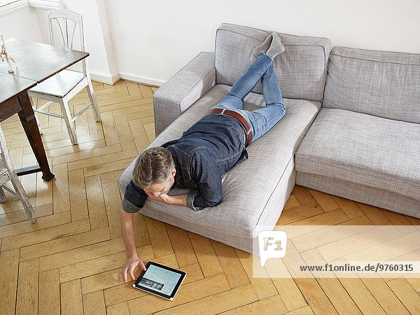 Erwachsener Mann auf dem Sofa liegend mit digitalem Tablett