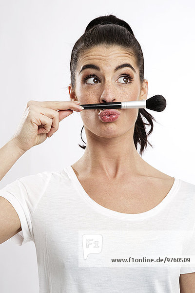 Porträt einer jungen Frau mit Schminkpinsel und schmollendem Mund