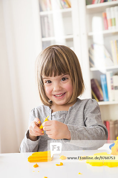 Portrait of happy little girl playing with yellow modeling clay