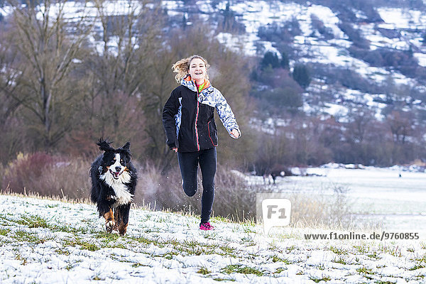 Germany  young woman jogging with her Saint Bernard on snow-covered meadow