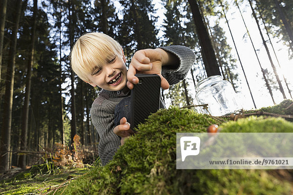 Deutschland,  lächelnder kleiner Junge beim Fotografieren der Natur im Wald