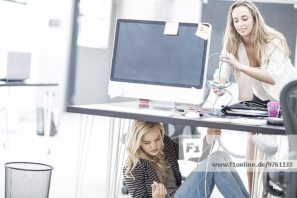 Kreative Bürofrauen  die versuchen  ein Netzwerkkabel unter ihrem Schreibtisch anzuschließen.