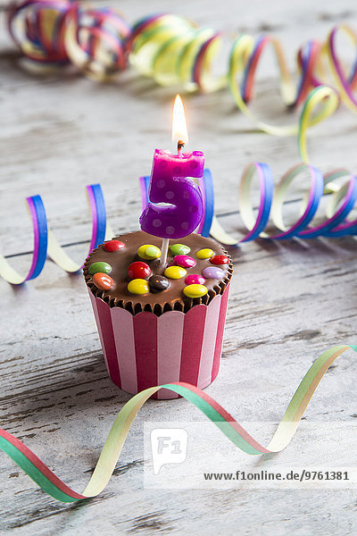 Geburtstagsmuffin mit Schokoladenknöpfen und angezündeter Kerze
