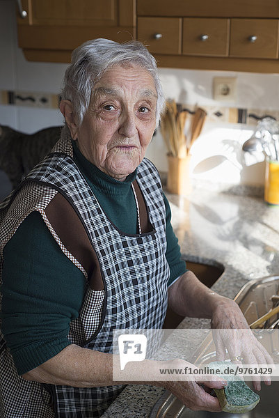 Porträt der Seniorin beim Geschirrspülen in der Küche