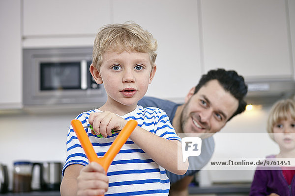 Little boy in kitchen learning to use slingshot