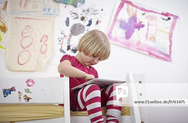 Little girl sitting on bunk bed  drawing on touch pad
