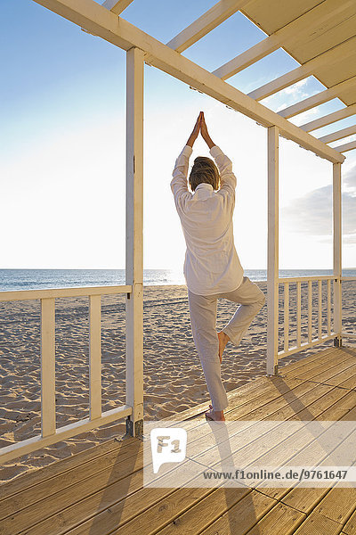 Portugal  Algarve  Frau beim Yoga am Strandhaus bei Sonnenuntergang