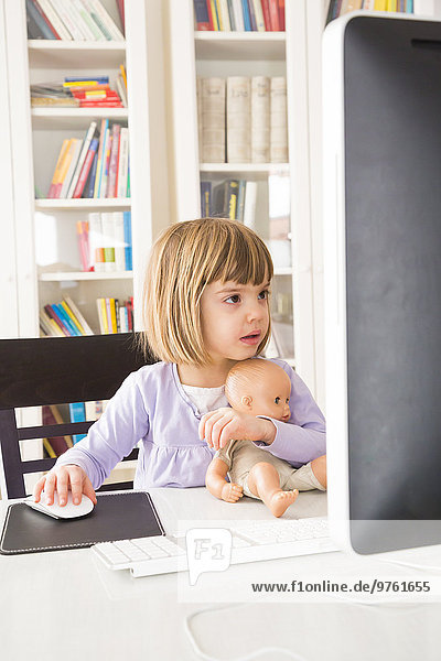 Portrait of little girl with doll spending time at computer