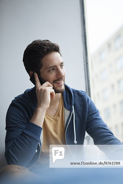 Portrait of smiling man telephoning with smartphone while looking through window