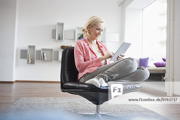 Frau entspannt sich mit digitalem Tablett auf Lederstuhl zu Hause