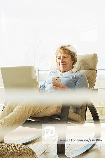 Senior woman at home using laptop and cell phone