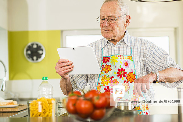Senior Mann mit digitalem Tablettenkochen in der Küche