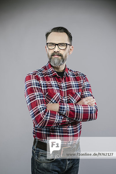 Porträt eines Mannes mit Bart und Brille  die die Arme kreuzen.