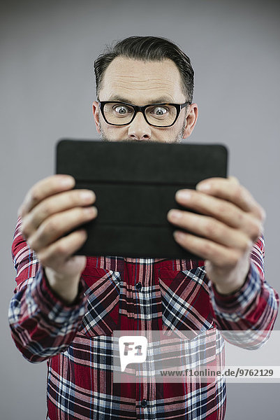 Mann mit weit geöffneten Augen schaut aufgeregt auf digitales Tablett
