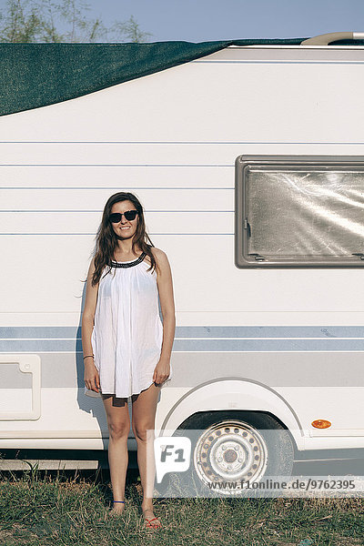 Junge Frau in Sommerkleidung vor dem Wohnwagen