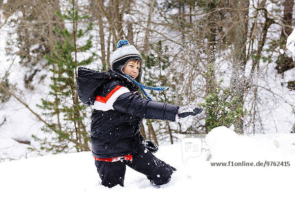 Glücklicher Junge spielt mit Schnee im Wald