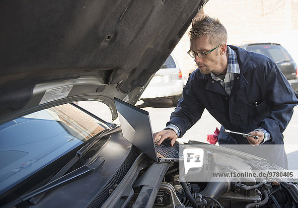 Mechanic using laptop while repairing car