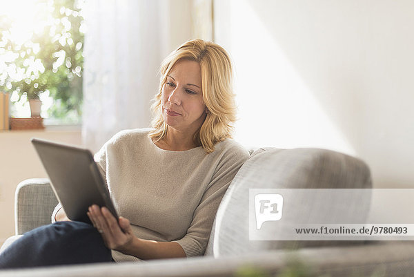 Woman sitting on sofa and using tablet pc