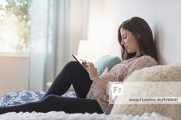 Pregnant woman sitting on bed using tablet