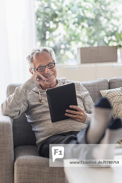 Senior man sitting on couch in living room  using tablet pc and smiling