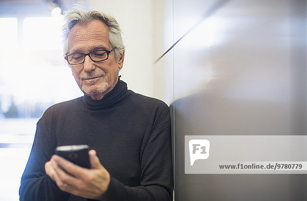 Senior man standing in office corridor and text messaging