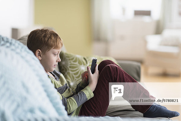 Boy (6-7) sitting on couch and using cell phone